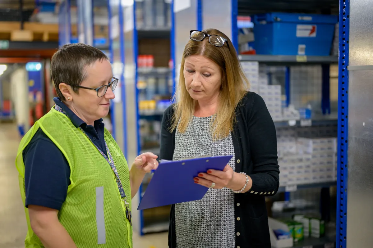 Two workers reviewing a clipboard together beside metal warehouse shelving.